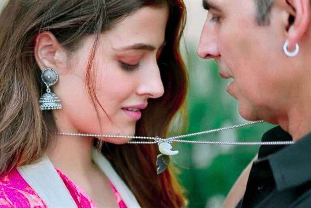 Akshay kumar and nupur sanon close up face to face holding a silver chain necklace in the song filhall